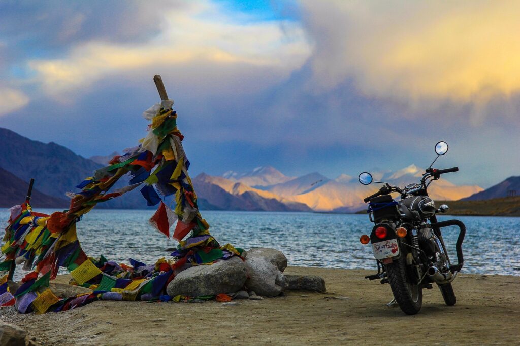 Scenic view of Pangong Lake in Ladakh with a motorcycle parked near colorful prayer flags, capturing the essence of an adventurous solo trip in the Himalayas.